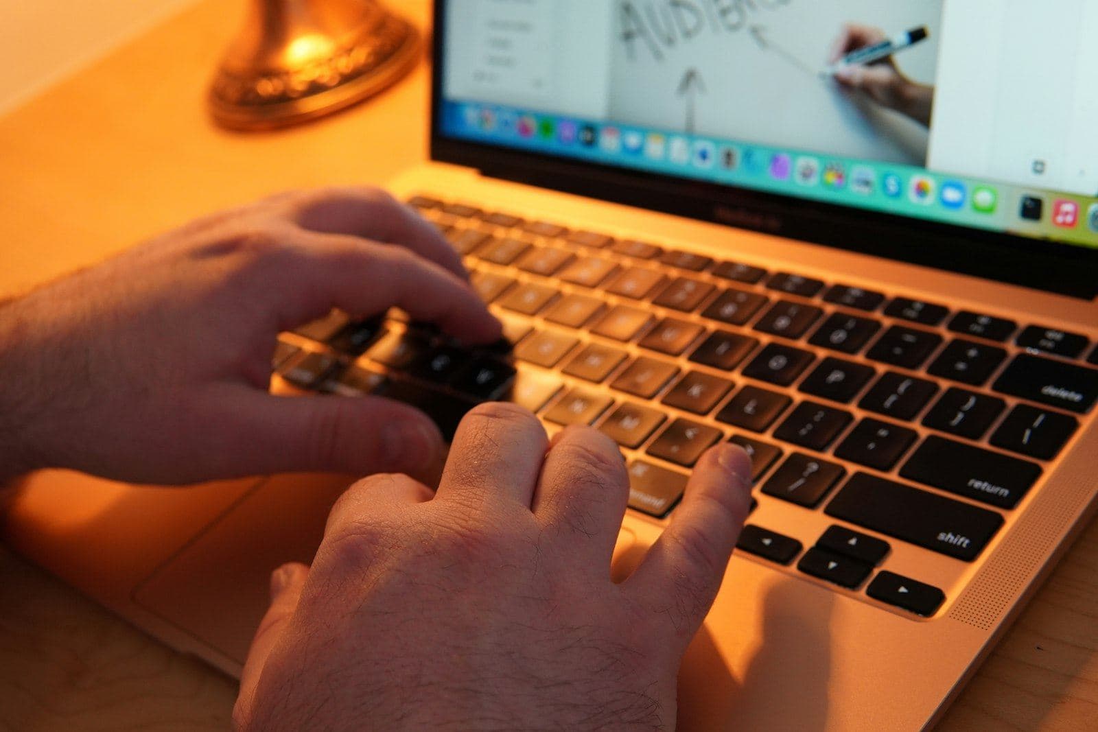 Hands typing on a laptop in warm lamp light